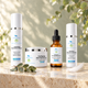 Stiltskin Renewal Ritual - Setophaga Restorative Cleanser, Cathartes Dermal Scrub, Antigone Skin Renewal Serum and Caladruis Daily Sun Protection on travertine with eucalyptus